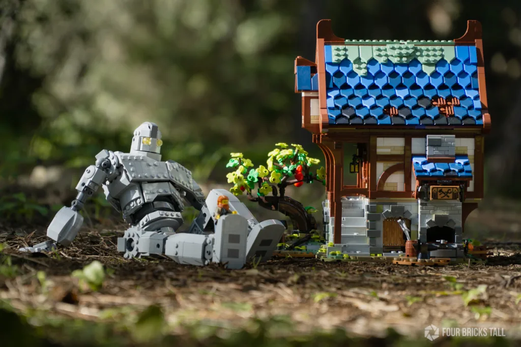 The Iron Giant getting a pedicure from a LEGO minfigure blacksmith in the forest. A LEGO blacksmith house is beside them.
