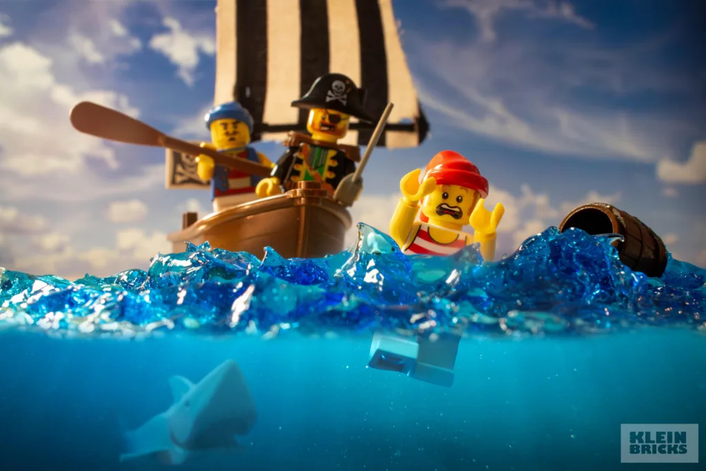 A distressed LEGO pirate minifig in the sea with a shark approaching and a small pirate boat behind