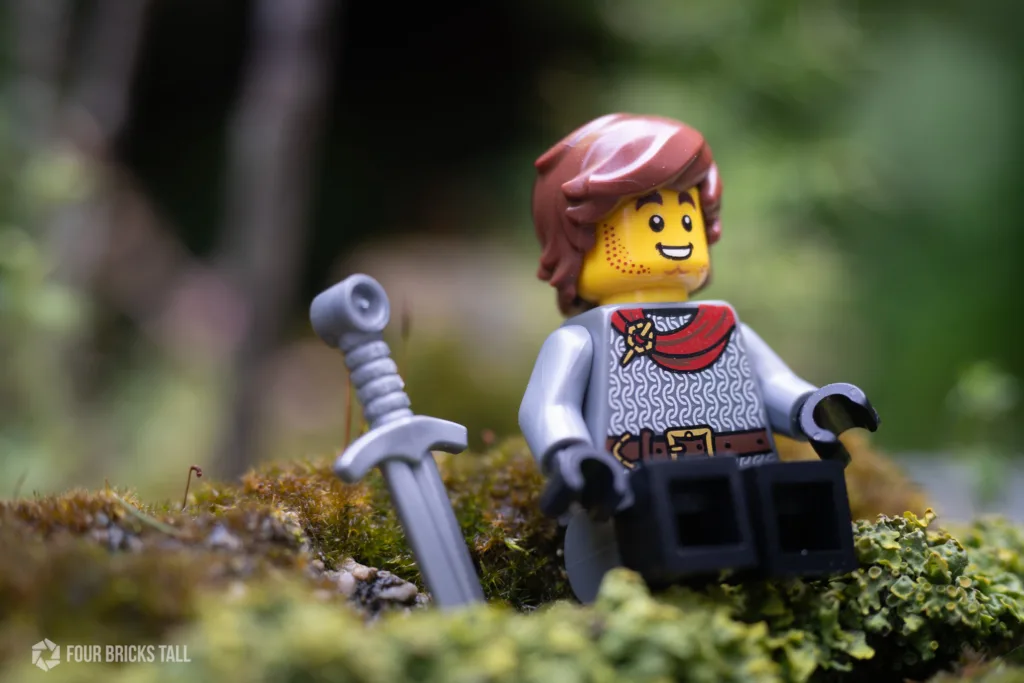 Medieval LEGO minifigure knight with sword sitting in moss. The torso is from BAM.